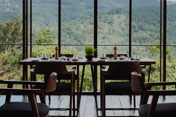 Wellness Resort Santani auf Sri Lanka. Hier Restaurant mit Holztischen und Stühlen, großer Fensterfront mit Blick auf bewaldete Berge