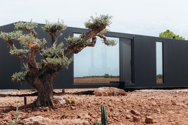 Ferienhaus District Hive in der Wüste von Granada. Containerartiger Bauklotz in Schwarz mit großen Fenstern auf steinigem Wüstenboden