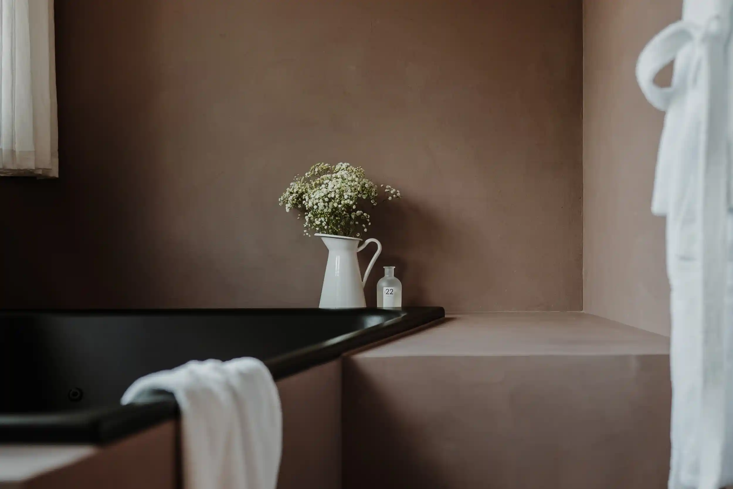 Atto Suites Südtirol: Badezimmer mit schwarzer Wanne und Blumen in einer Vase vor rotbraun gestrichener Wand