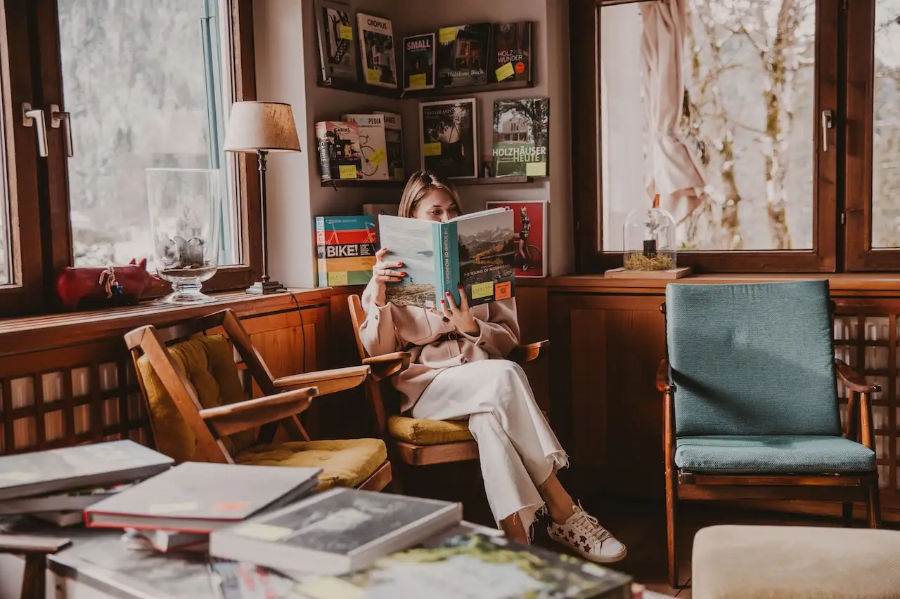Hotel Seebichl: Frau, die ein Coffee-Table-Book durchblättert auf altem 70er Jahre Sessel, drumherum weitere Bücher und zwei weitere alte Sessel