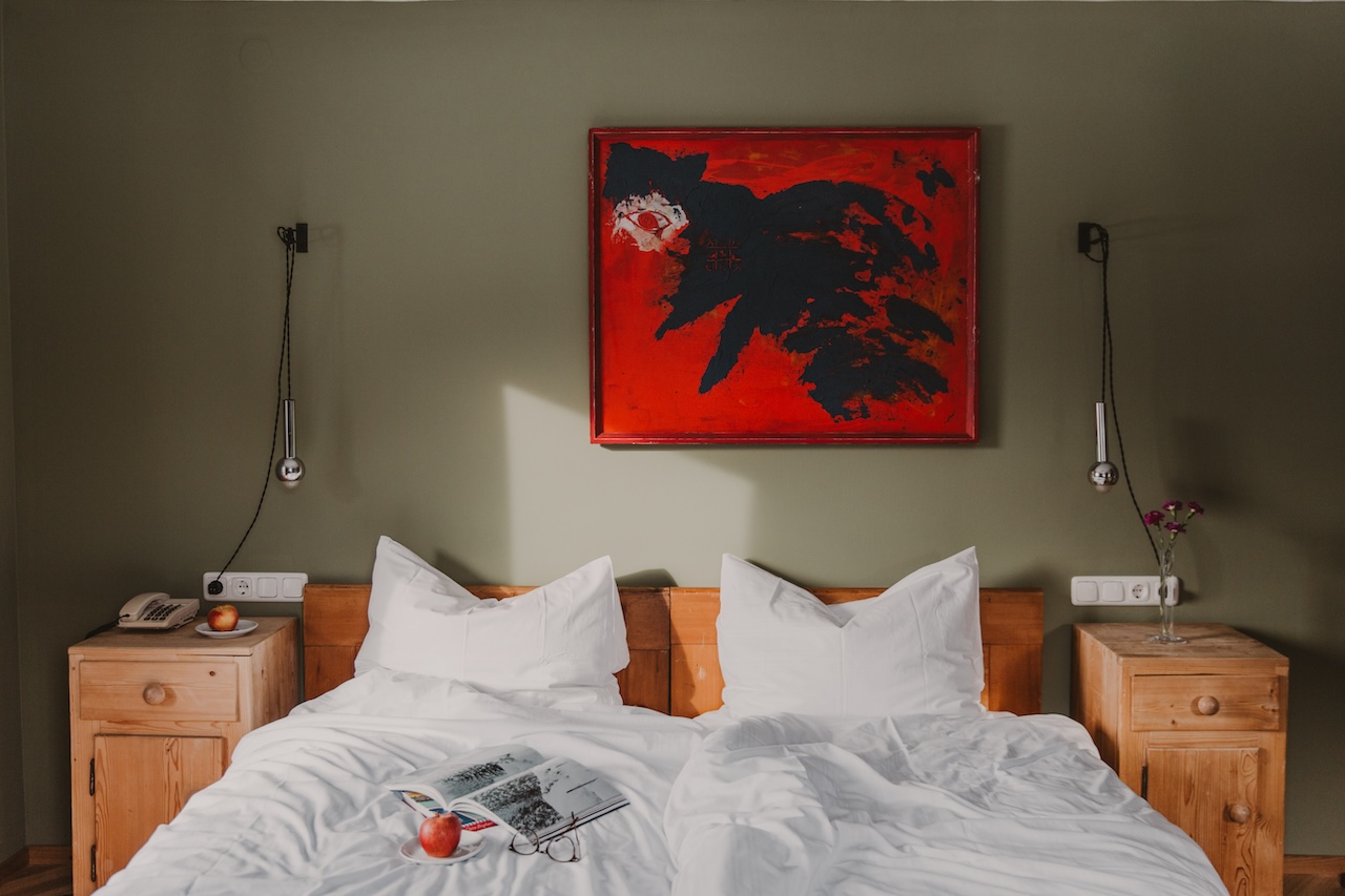 Schlafzimmer mit Doppelbett im Hotel Seebichl, helle Laken, Bett aus Holz, grüne Wand, rotes Bild über dem Bett