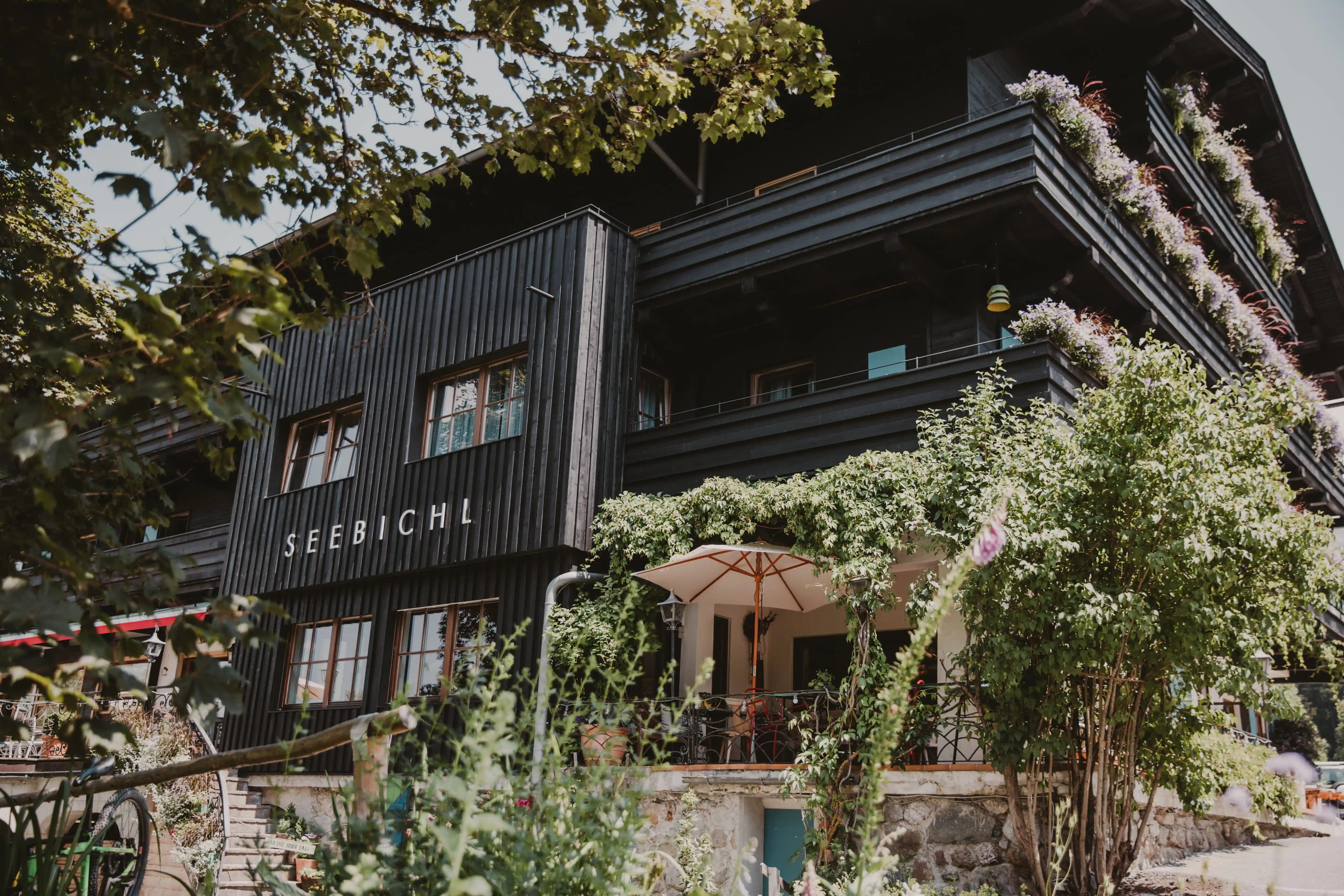 Außenansicht vom Hotel Seebichl: Dunkle Holzfassade, Blumen und Schriftzug „Seebichl“