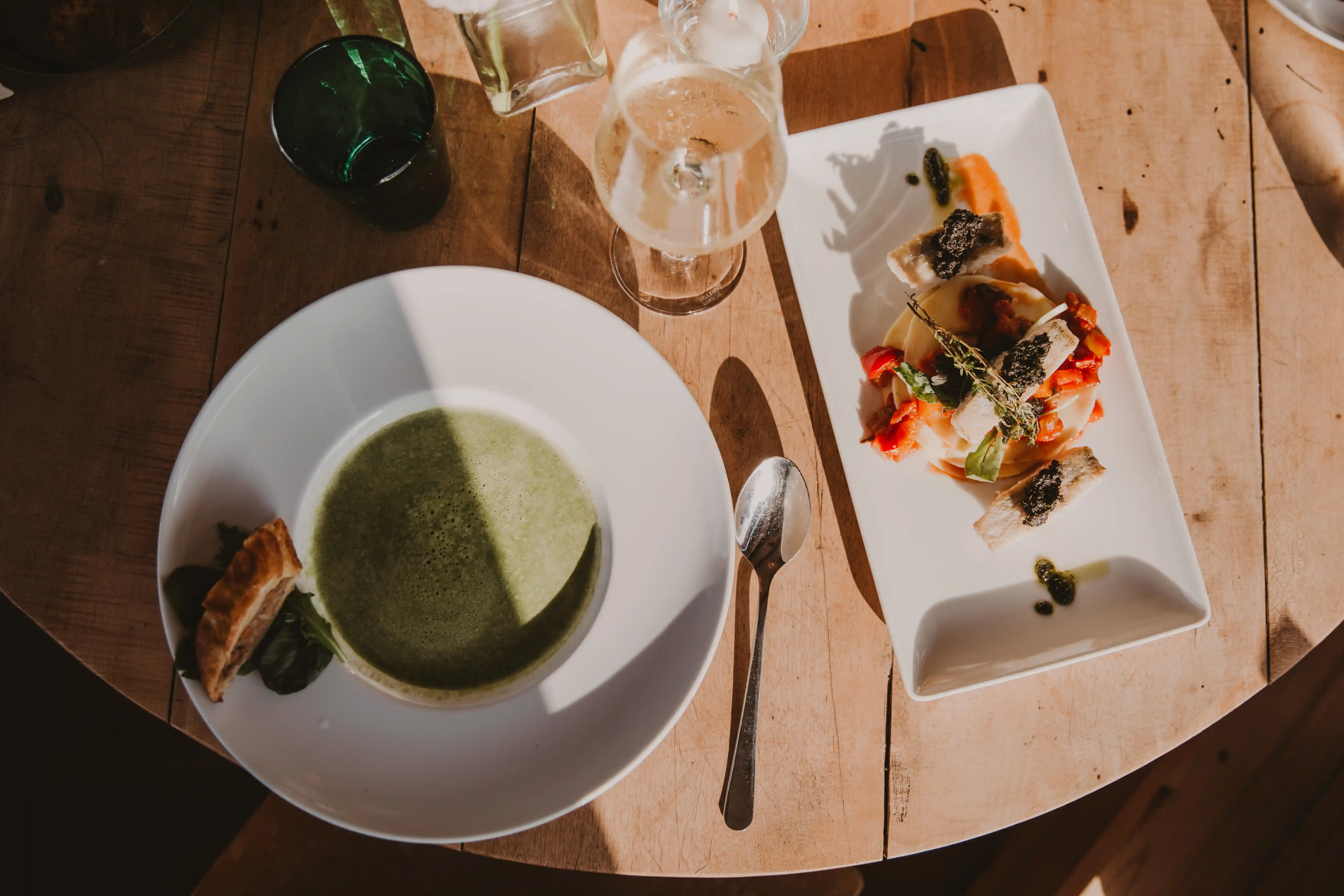 Grüne Suppe, ein Glas Weißwein und Salat auf rundem Holztisch
