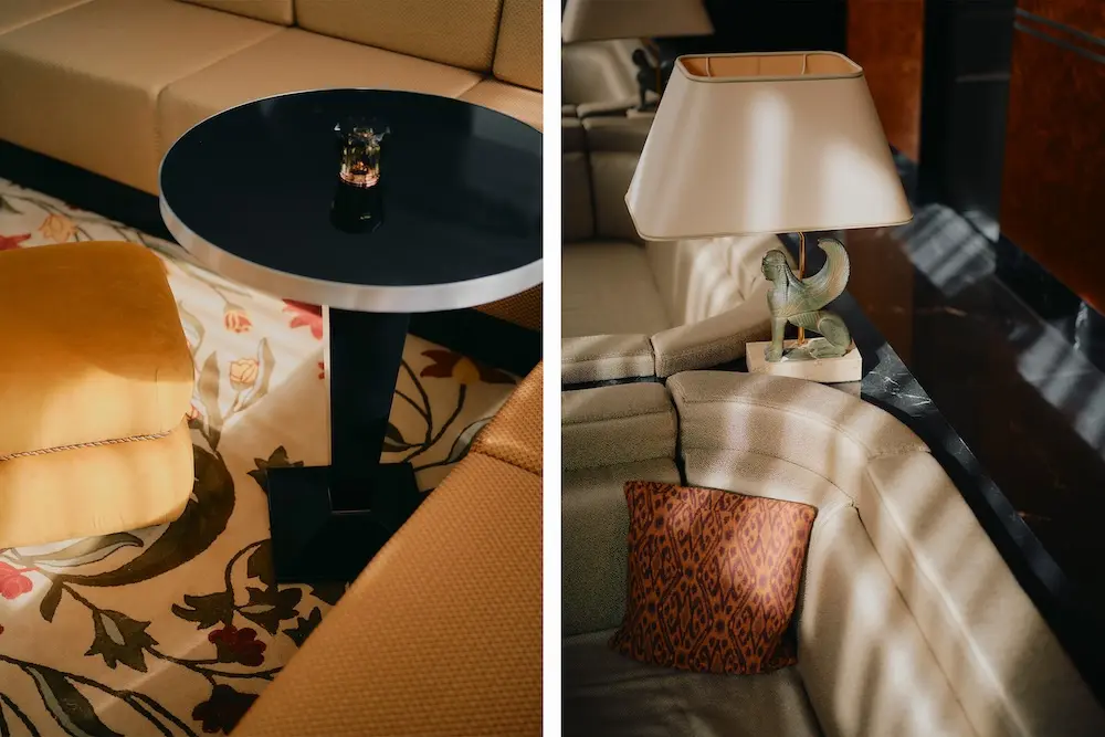 Jugendstil-Elemente in der Lounge des Hotels The Dean Munich: Schwarzer runder Beistelltisch, gelbes Sofa, Lampe mit Sphinx