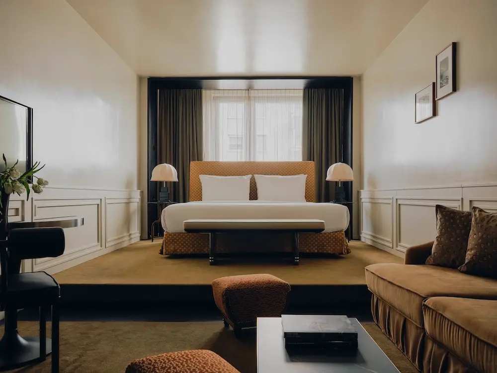 Junior Suite im The Dean Munich: Ockerfarbener Teppich, braunes Sofa, gelbes Bett, dunkelgrüne Vorhänge