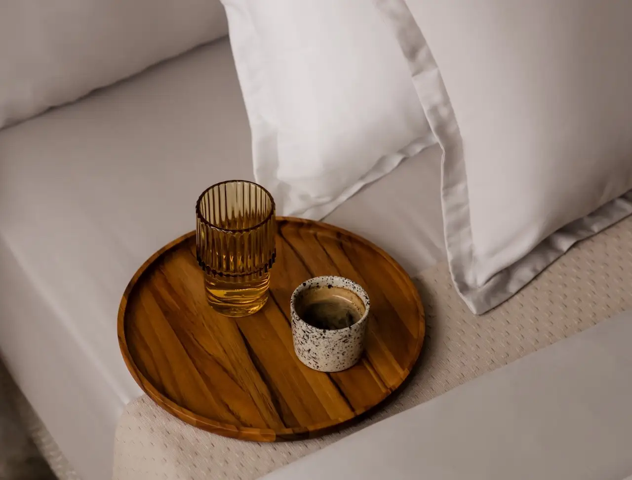 Holzbrett mit Kaffee und Wasser auf Bett mit beigefarbener Bettwäsche Amqua