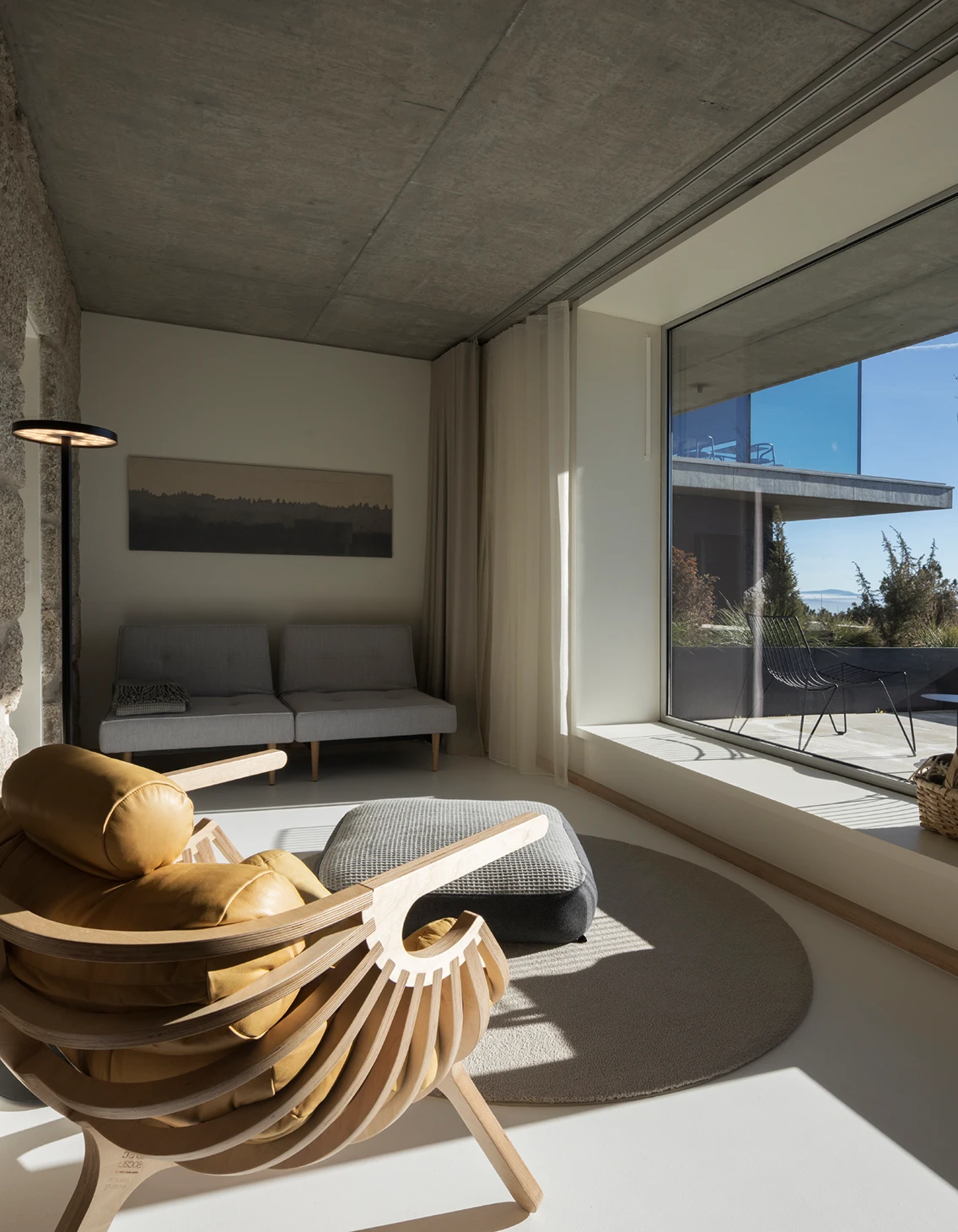 Sonnige Leseecke im Hotelzimmer mit Leder-Designsessel, weitem Ausblick und hellem Terrazzoboden.