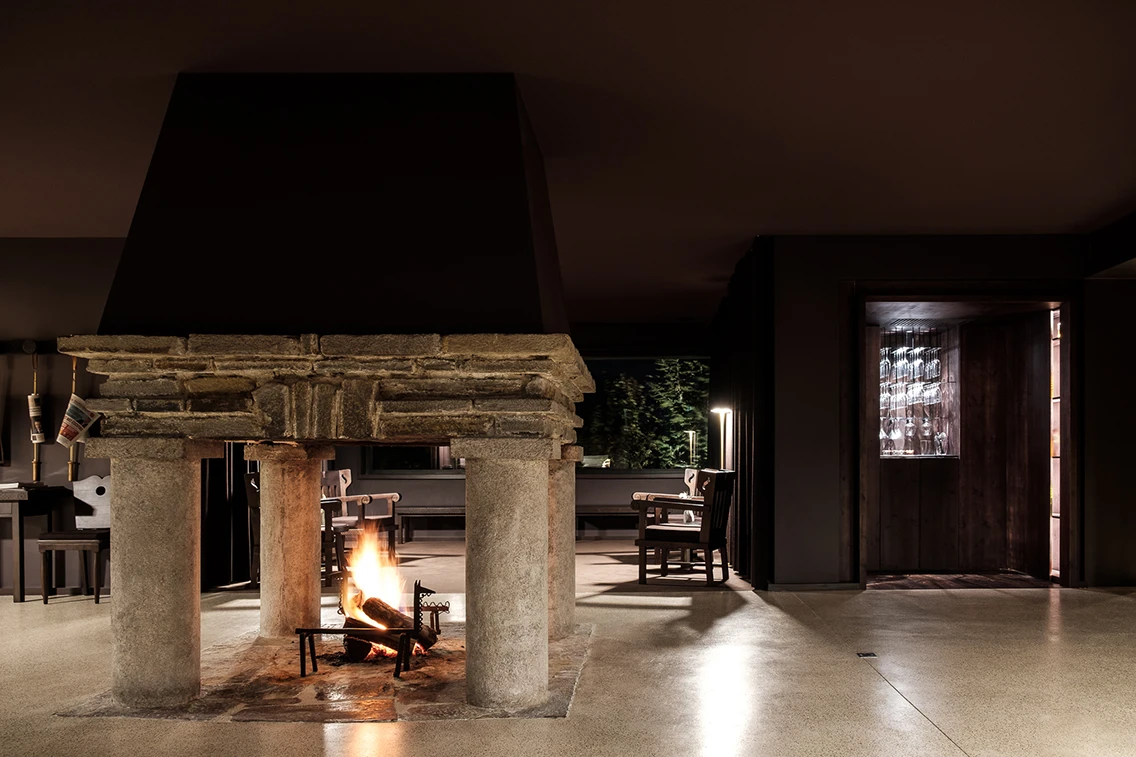 Historischer, offener Kamin aus Naturstein im gemütlich beleuchteten Lounge-Bereich des Berg-Designhotels.