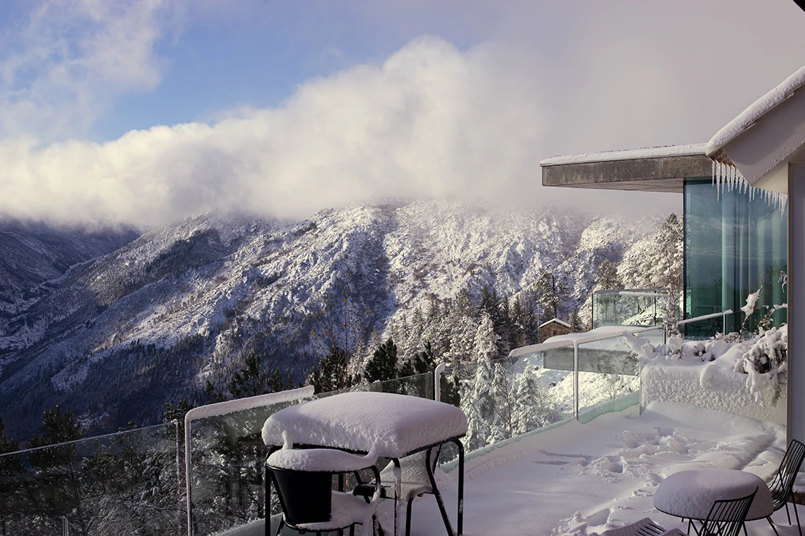Die verschneite Terrasse des Hotels Casa de São Lourenço im Winter mit weitem Blick über die schneebedeckten Berggipfel und Pinienwälder.