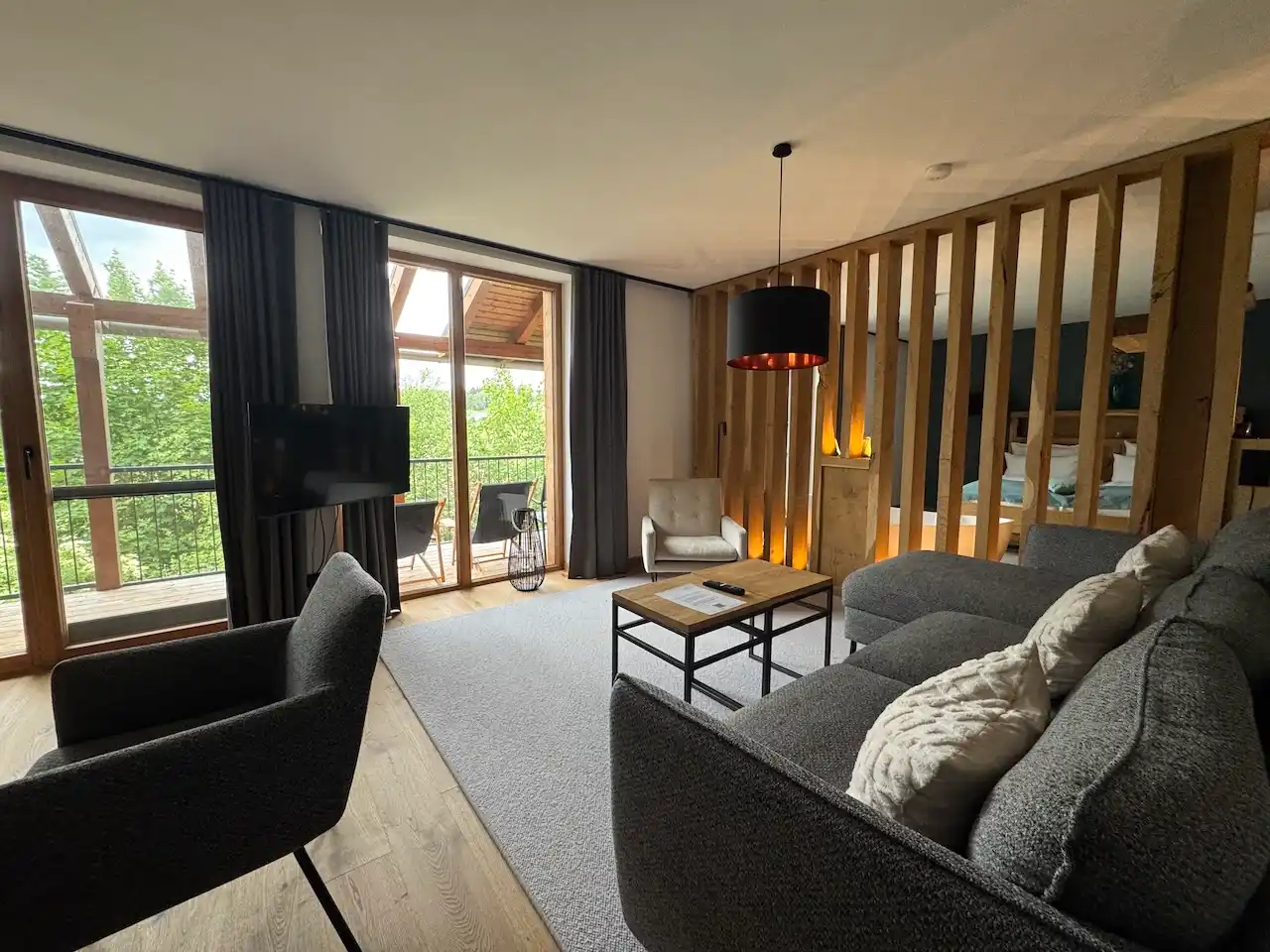 In einer der Suiten im FORSTGUT, graues Sofa, Trennwand aus Holzpaneelen 