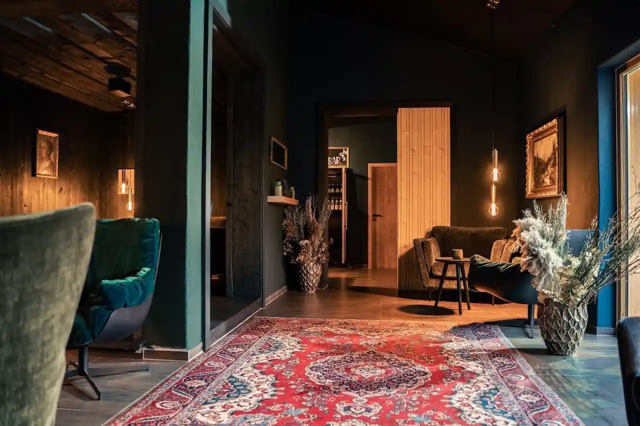 Im FORSTGUT: Deep Green Lounge mit buntem Teppich, Sesseln und Holzwänden