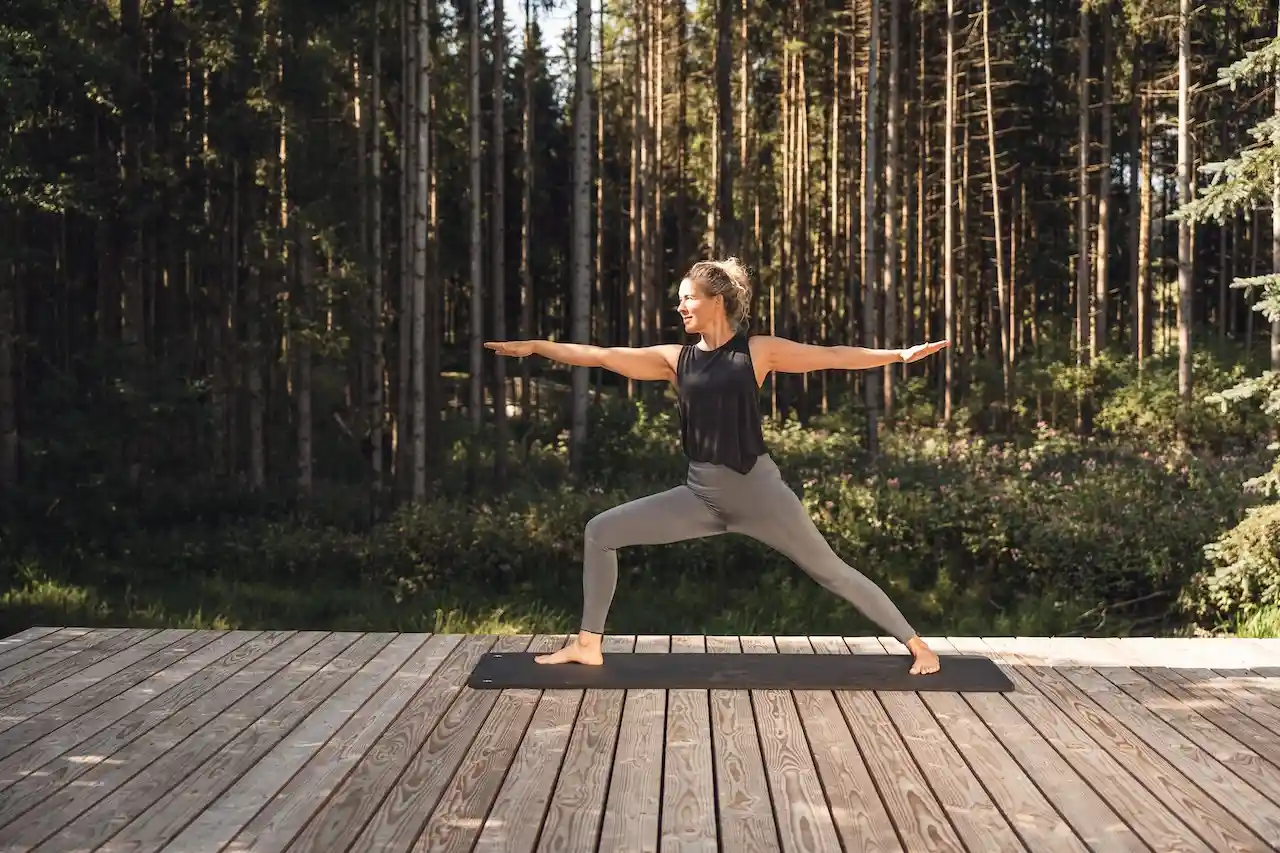 Frau, die Yoga auf einer Holzplattform im Wald macht