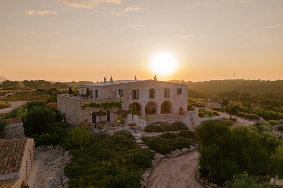 Außenansicht des Boutique-Hotels Son Blanc Farmhouse auf Menorca mit Natursteinfassade, Bogenfenstern und Außenterrasse bei warmem Sonnenuntergangslicht.