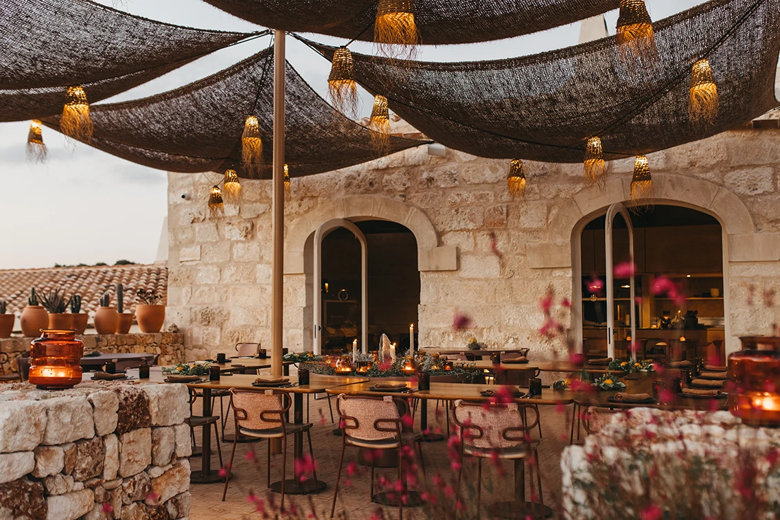 Stimmungsvolle Restaurant-Außenterrasse im Son Blanc Farmhouse Menorca mit Sonnensegeln, gewebten Lampions, eingedeckten Holztischen und Kerzenschein.