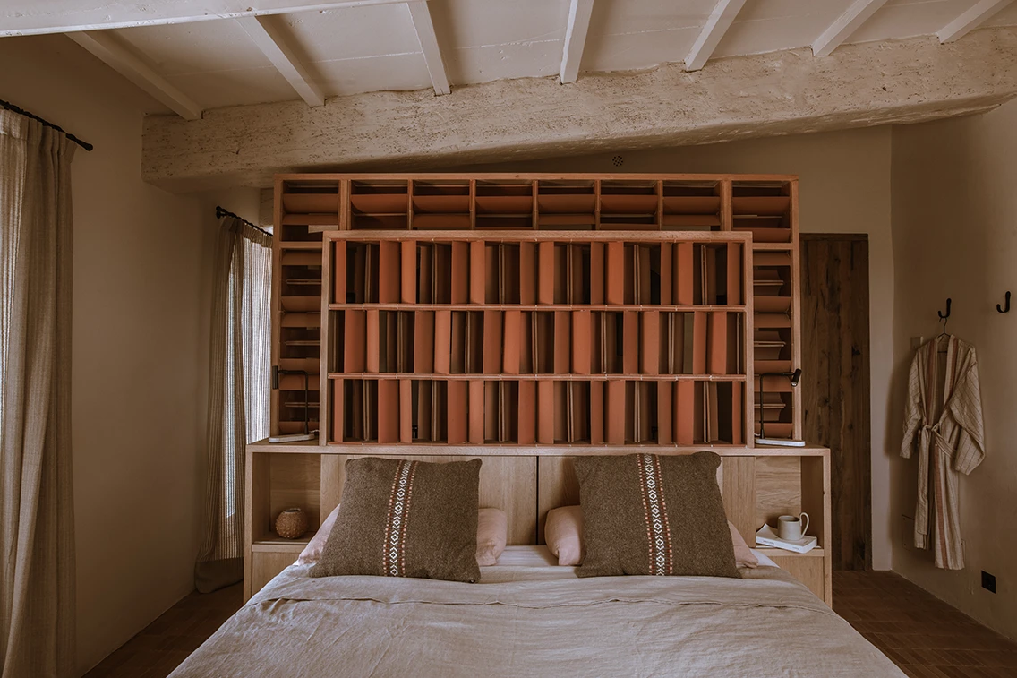 Doppelbett im Son Blanc Farmhouse Menorca mit maßgefertigter Holz- und Terrakotta-Rückwand als Raumteiler sowie freiliegenden Holzbalken.
