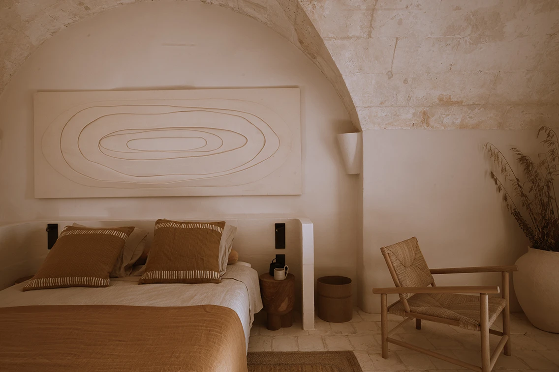 Stilvolles Doppelzimmer unter historischem Tonnengewölbe im Son Blanc Farmhouse Menorca mit erdfarbenem Bettzeug, Relief-Kunstwerk und Holzstuhl.