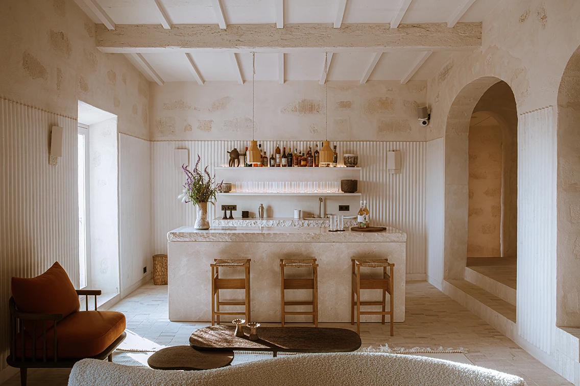 Bar- und Loungebereich im Son Blanc Farmhouse Menorca mit hellem Natursteintresen, Barhockern aus Holz und eleganten Rundbögen.
