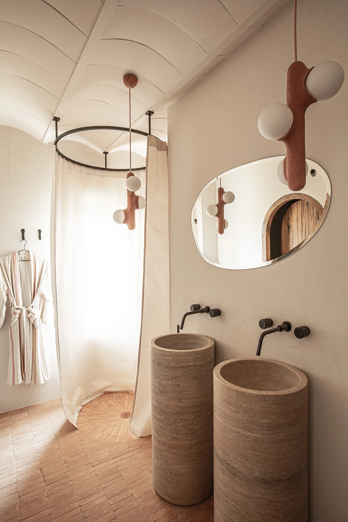 Minimalistisches Hotelbad im Son Blanc Farmhouse Menorca mit zwei zylinderförmigen Steinwaschbecken, organischem Wandspiegel und Design-Pendelleuchte.