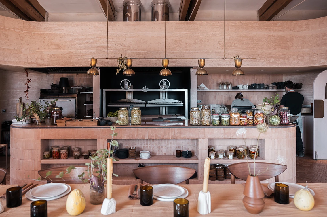 Offene Küche im Restaurant des Son Blanc Farmhouse Menorca mit Terrakotta-Tresen, Einmachgläsern, Messing-Pendelleuchten und großem Holzkohlegrill.