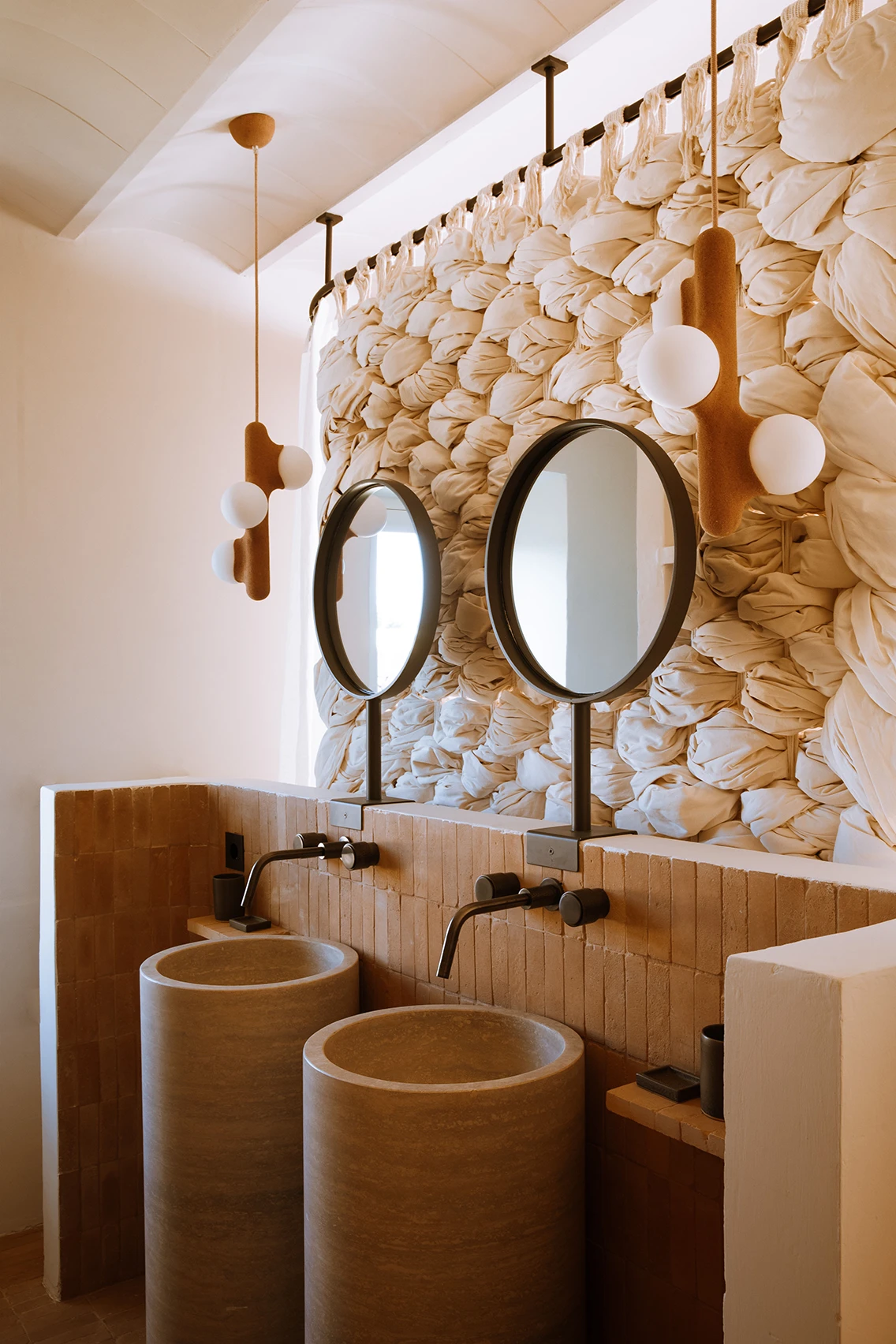 Modernes Hotelbadezimmer im Son Blanc Farmhouse Menorca mit zwei zylinderförmigen Steinwaschbecken, runden Spiegeln und einer gewebten Textil-Installation.