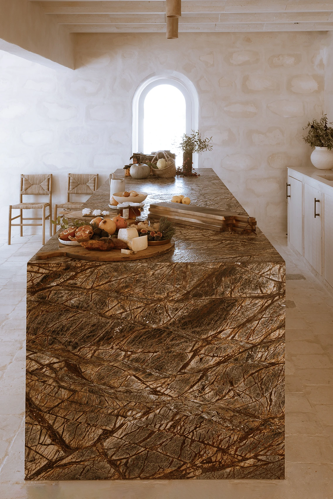 Massiver Küchenblock aus gemustertem braunem Naturstein im Son Blanc Farmhouse Menorca, angereichert mit frischen Früchten, Käse und Brot.