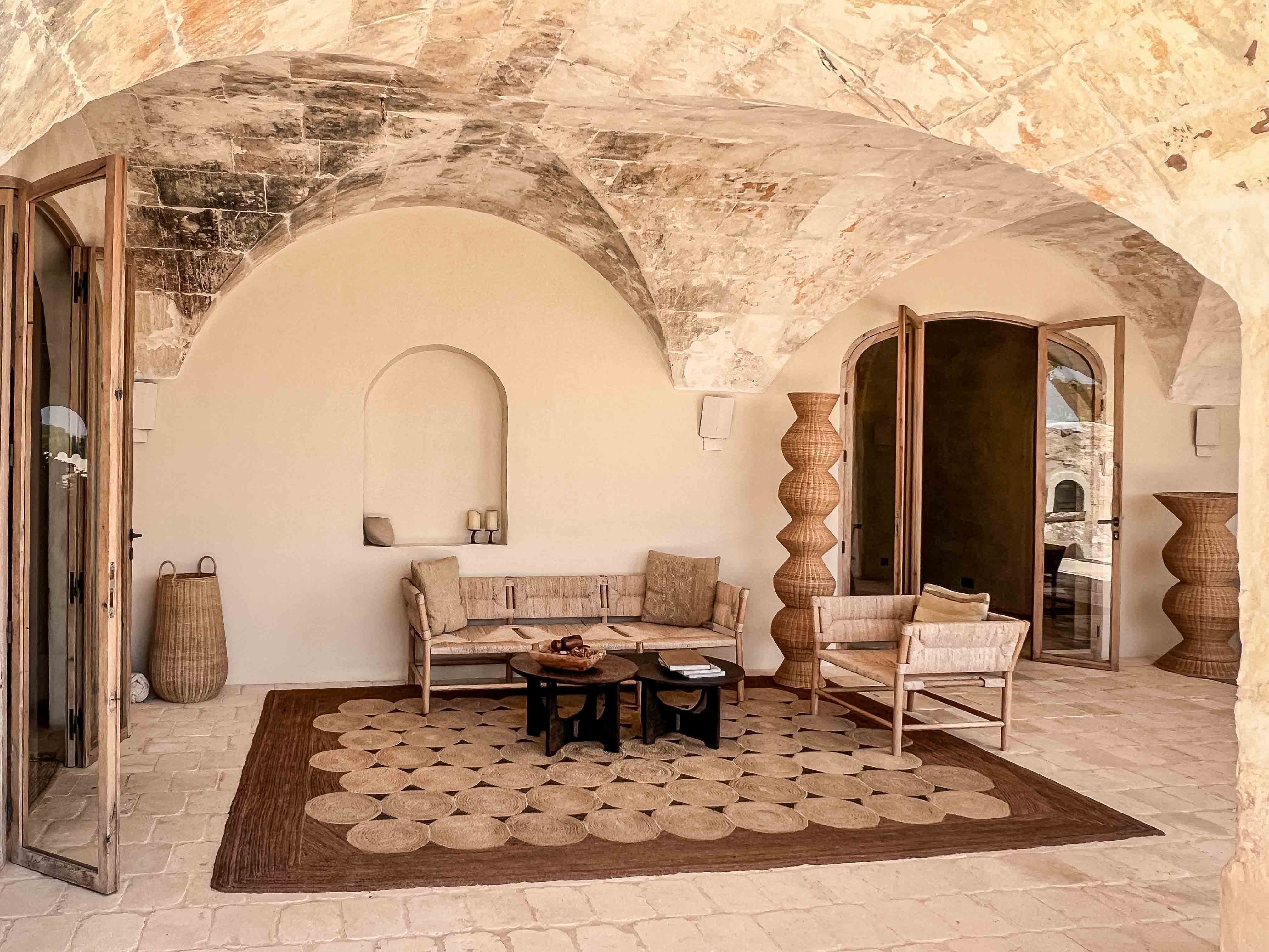 Überdachter Lounge-Eingangsbereich im Son Blanc Farmhouse Menorca mit historischem Gewölbe, Flechtsofas, Teppich und Rattandekor.