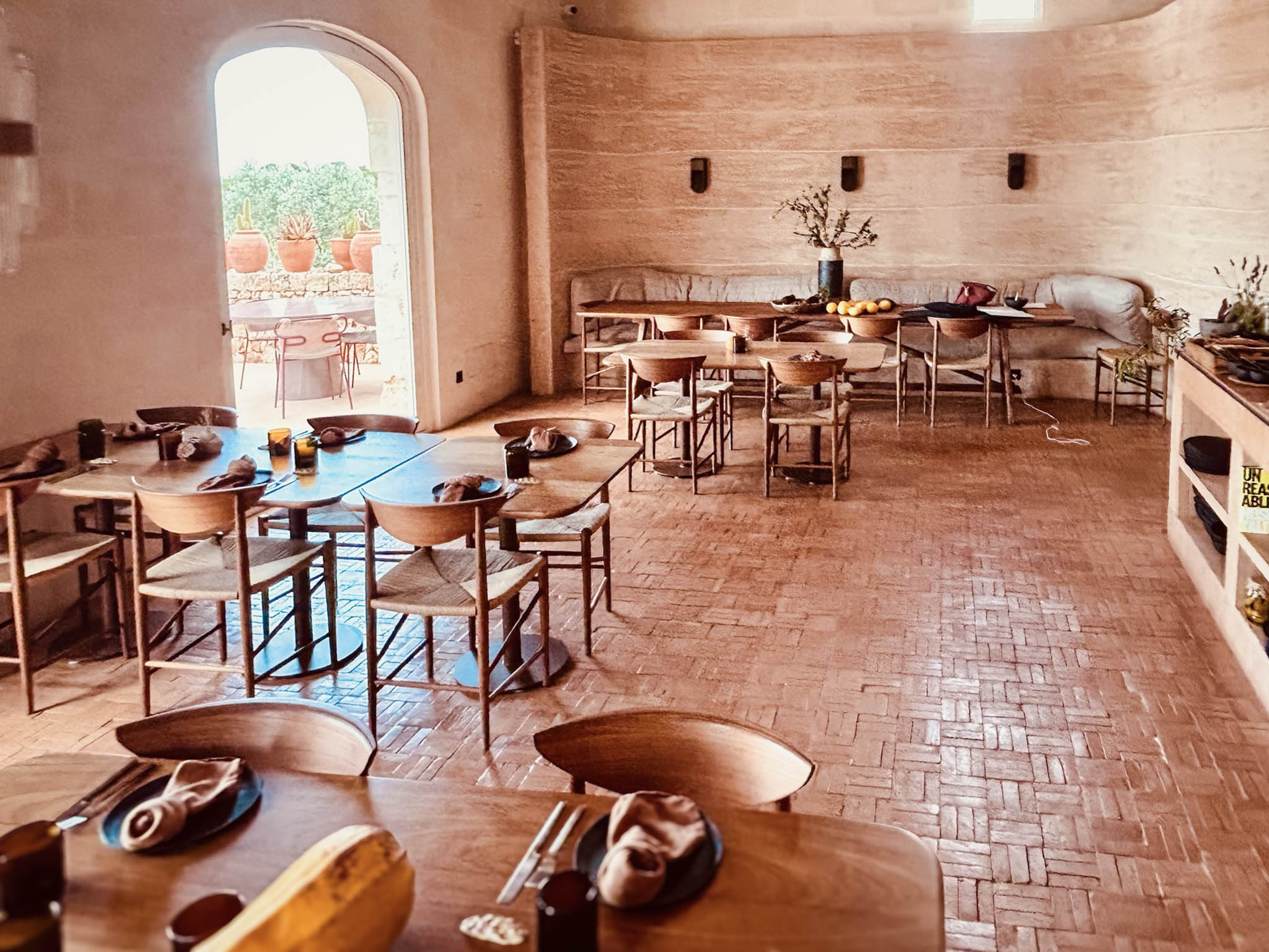 Lichtdurchfluteter Gastraum im Restaurant des Son Blanc Farmhouse Menorca mit Holzmobiliar, Cotto-Boden und Rundbogen-Durchgang zur Terrasse.