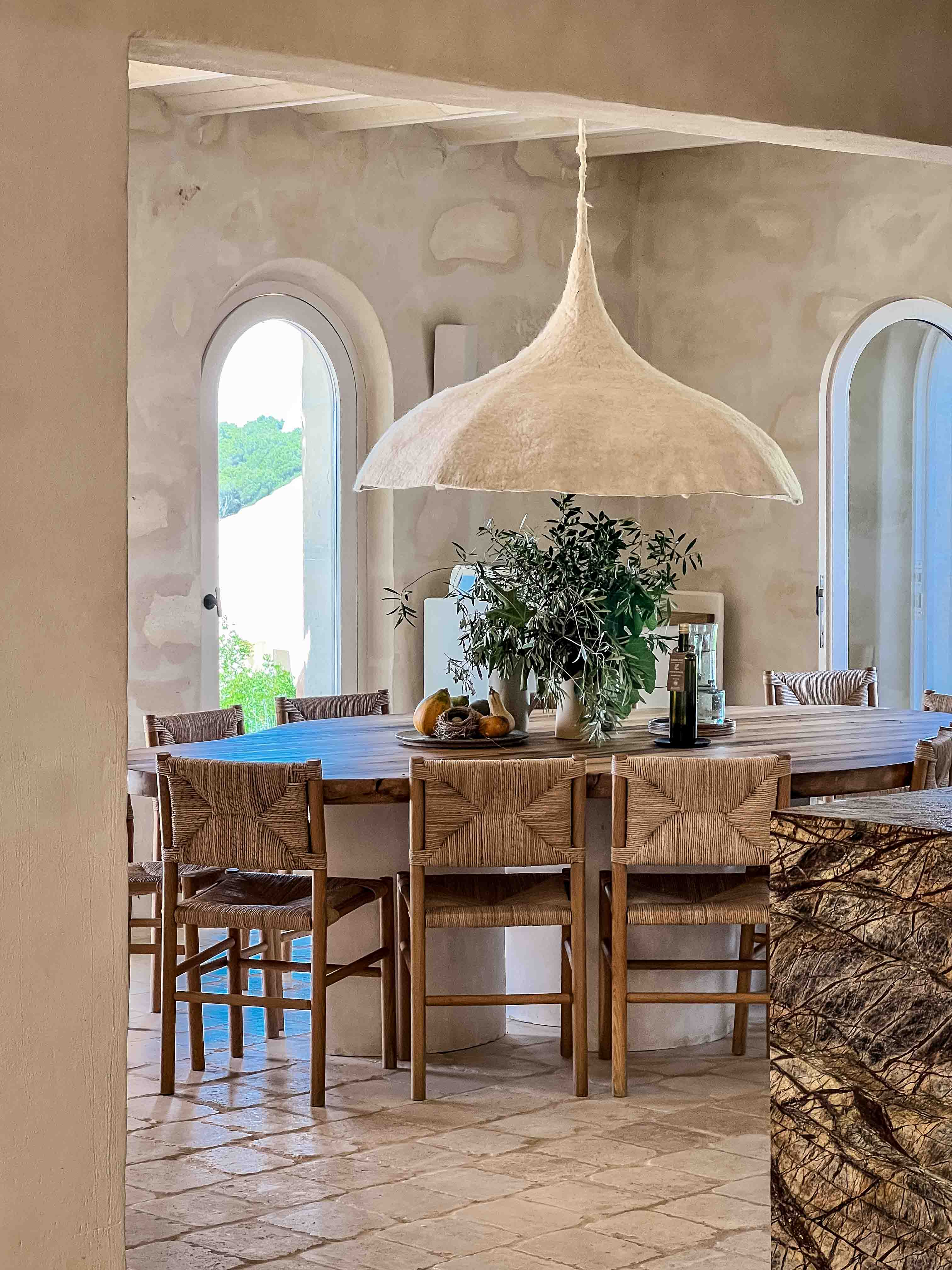 Ovaler Massivholztisch mit Flechtstühlen und skulpturaler Hängeleuchte im mediterranen Innenraum des Son Blanc Farmhouse Menorca.