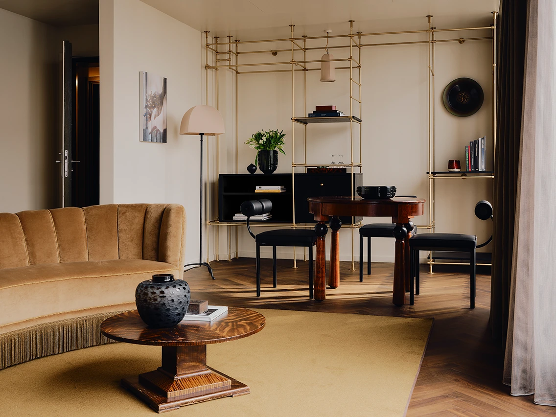Großzügiges Wohnzimmer einer Suite mit Parkettboden, Samtsessel, Messingregal und Designerstühlen im Hotel The Dean München