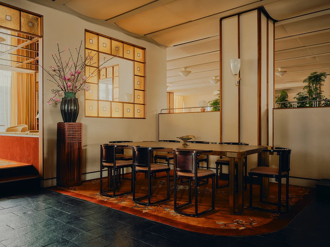 Langer Esstisch aus Holz mit Designstühlen und großer Blumenvase vor verglaster Trennwand im Restaurant Ibasho im The Dean München