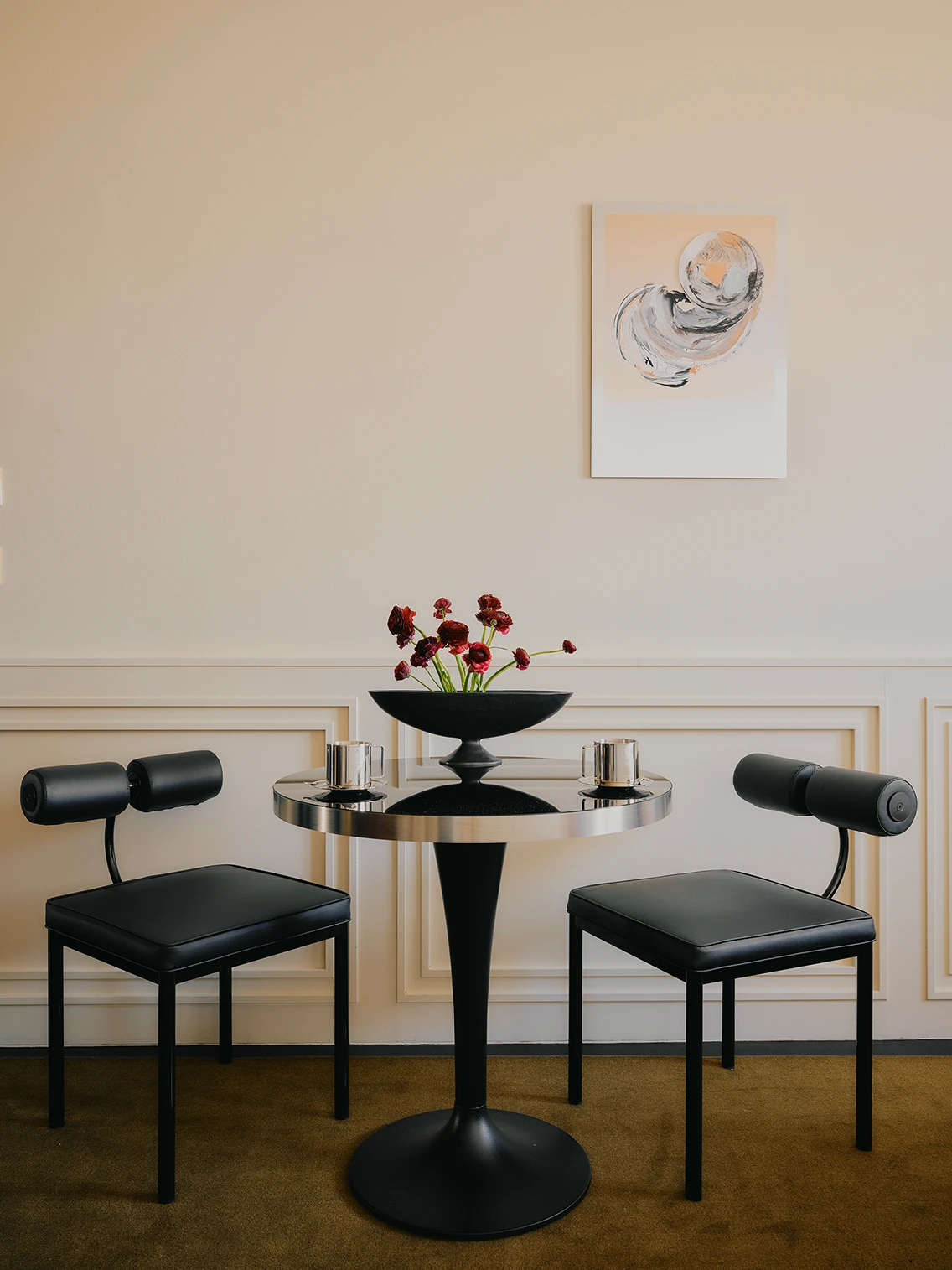 Minimalistische Sitzecke mit rundem Bistrotisch, schwarzen Designstühlen und Kunstwerk an der Wand im Hotel The Dean München