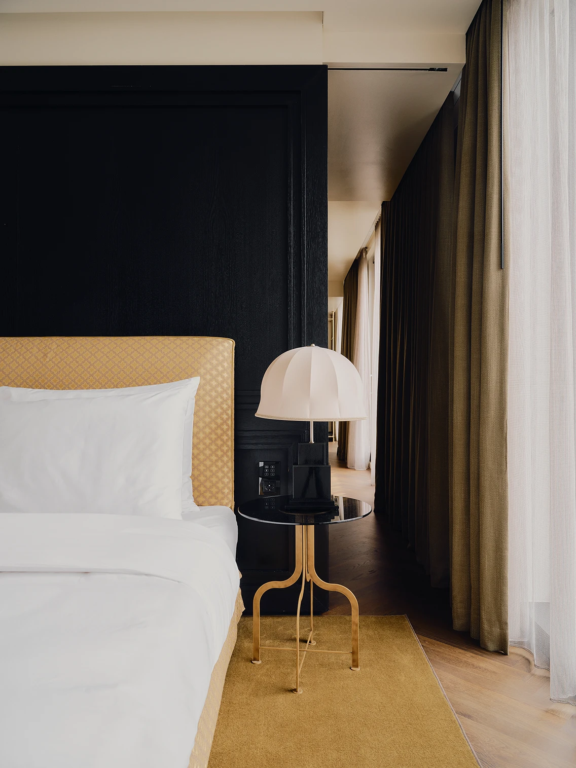 Detailansicht des Kingsize-Betts mit gelb gemustertem Kopfteil, Designer-Tischleuchte und Vorhängen im Zimmer des The Dean München