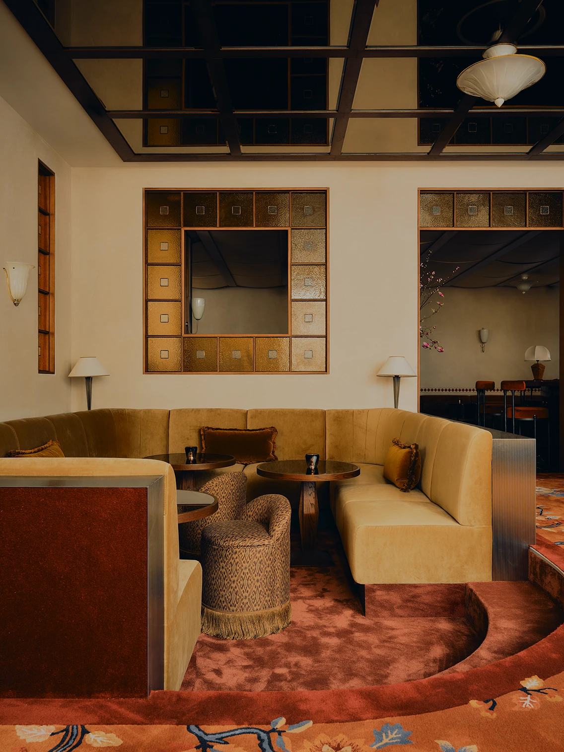Eingebettete Nische mit ockerfarbenem Samtsofa, gepolstertem Hocker und Teppich im Loungebereich des Ibasho Restaurants im The Dean München