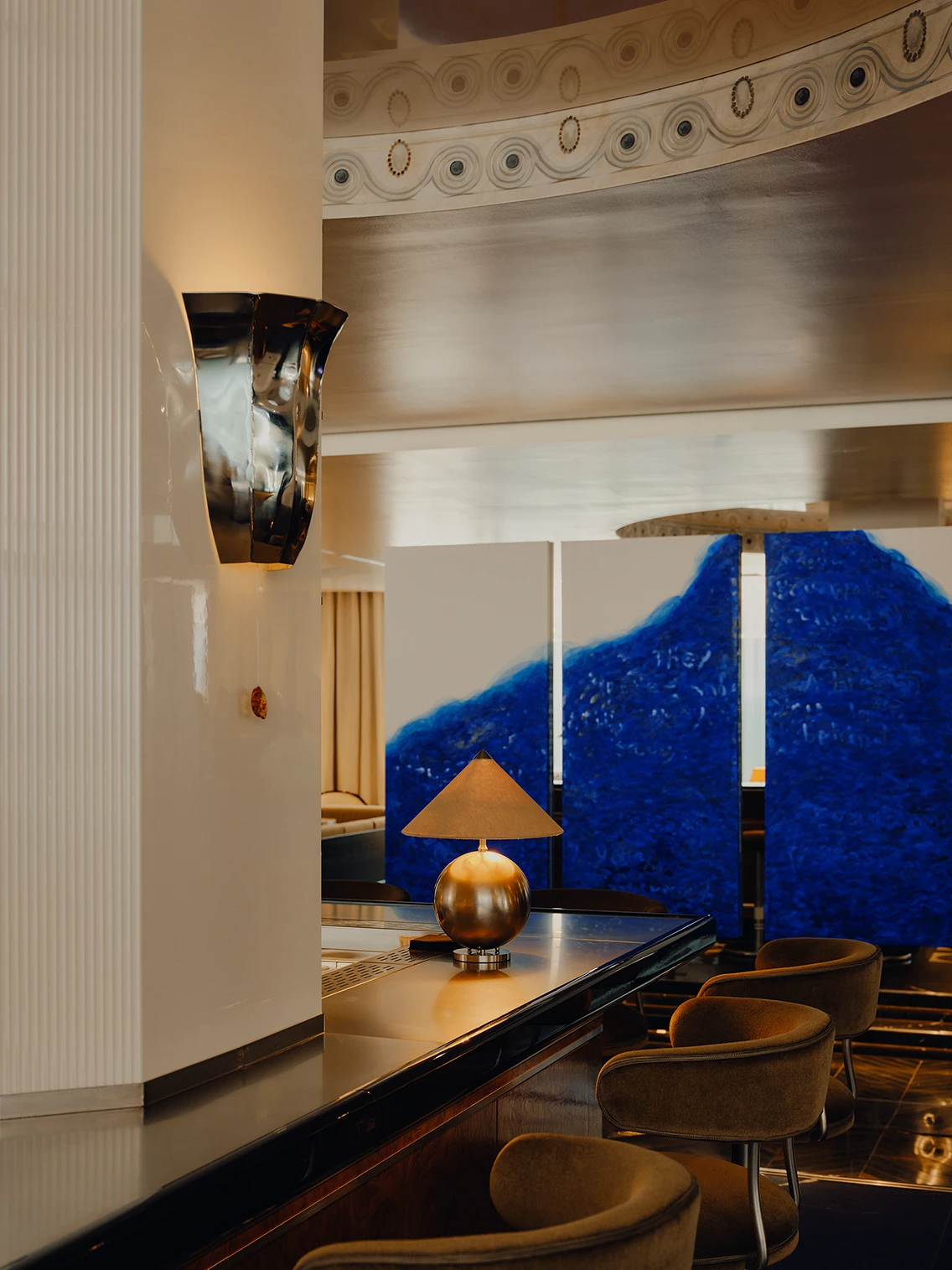 Blaues dreiteiliges Kunstwerk hinter der Hotelbar und messingfarbene Tischleuchte in der Lobby des Hotels The Dean München