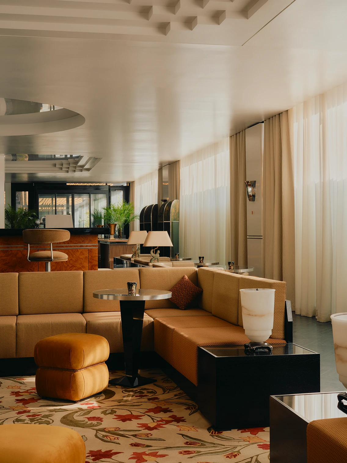 Großzügiges gelbes Ecksofa mit gepolstertem Hocker, Beistelltisch und bedrucktem Teppich in der lichtdurchfluteten Lobby des Hotels The Dean München