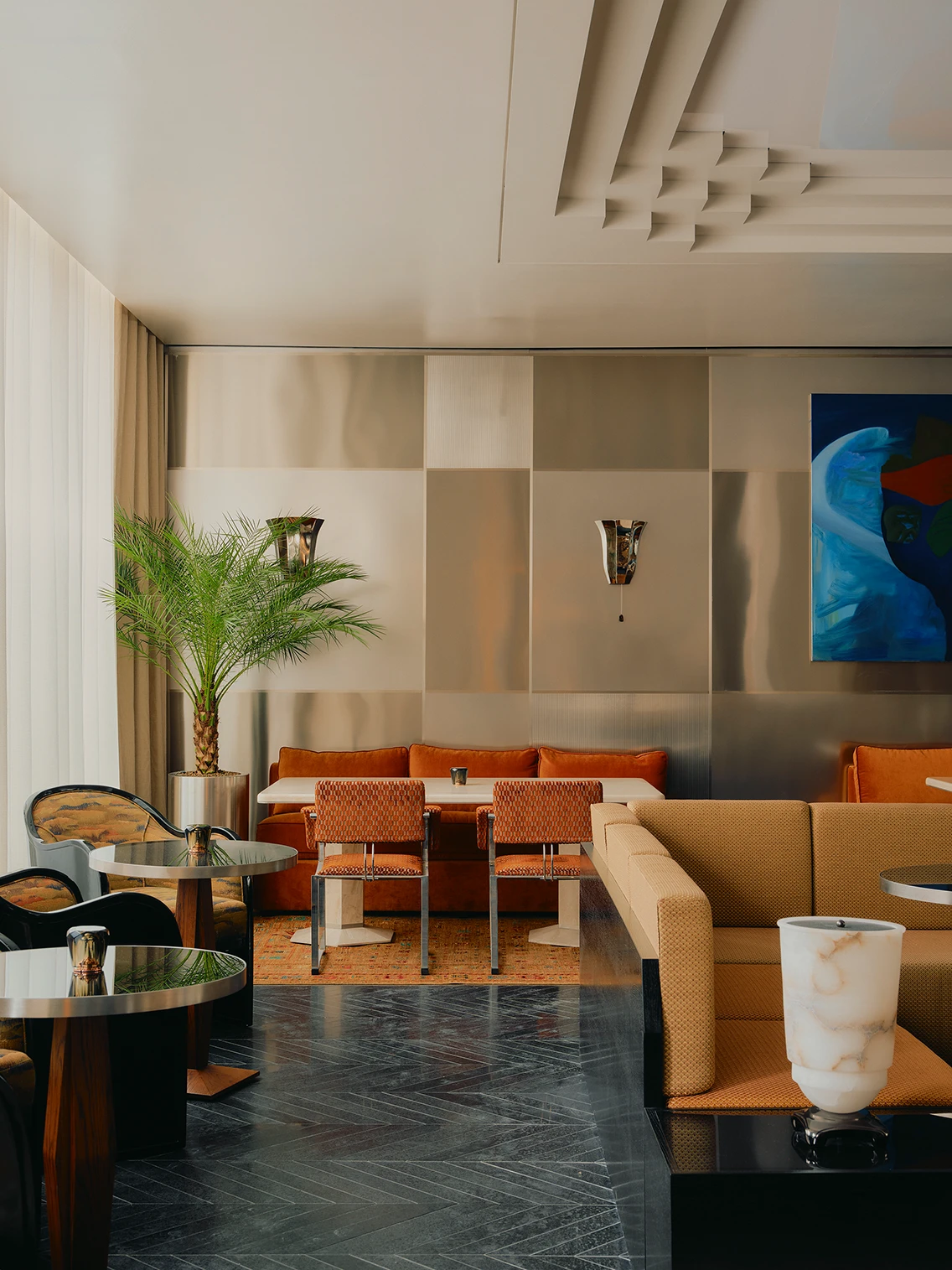Eklektischer Loungebereich mit Edelstahl-Wandverkleidung, rotem Samtsofa, Bistrotischen und Zimmerpflanze im Hotel The Dean München