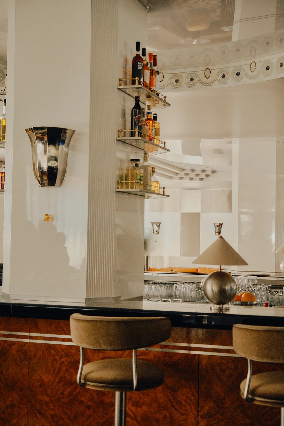 Elegante Bar-Theke aus Holz mit samtigen Barhockern, Barspiegel und Spirituosenregal in der Lobby des Hotels The Dean München