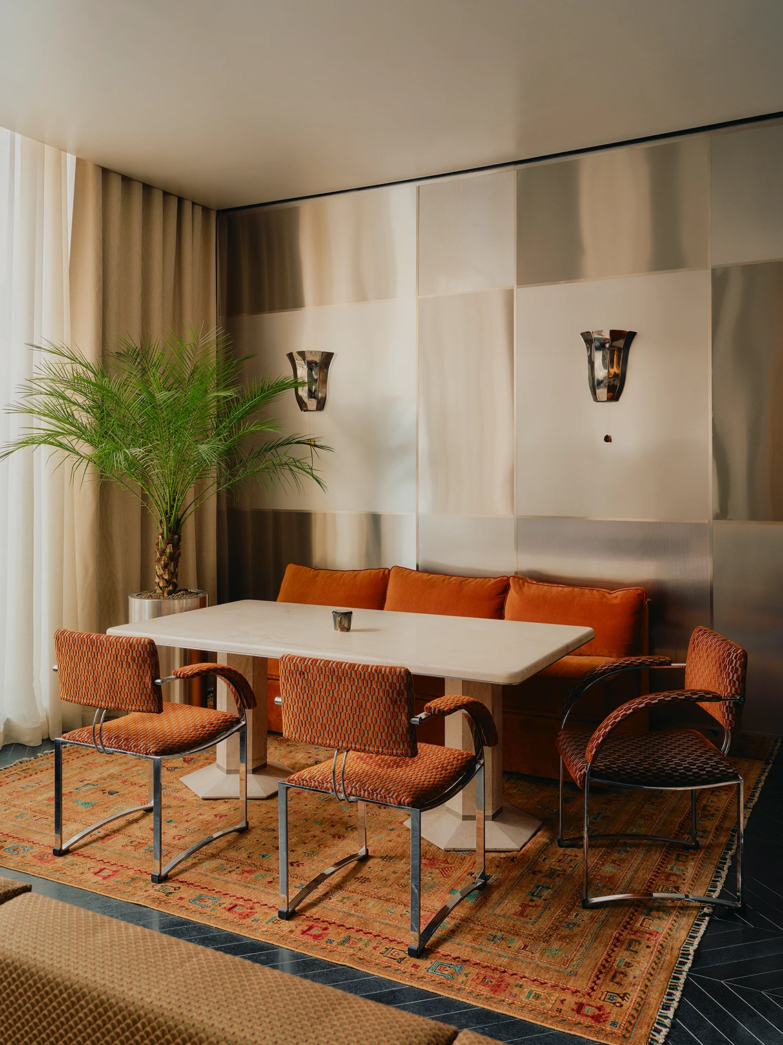 Retro-Sitzecke in der Lobby des Hotels The Dean München mit rotem Samtsofa, Designer-Sesseln, Teppich und Edelstahl-Wandverkleidung