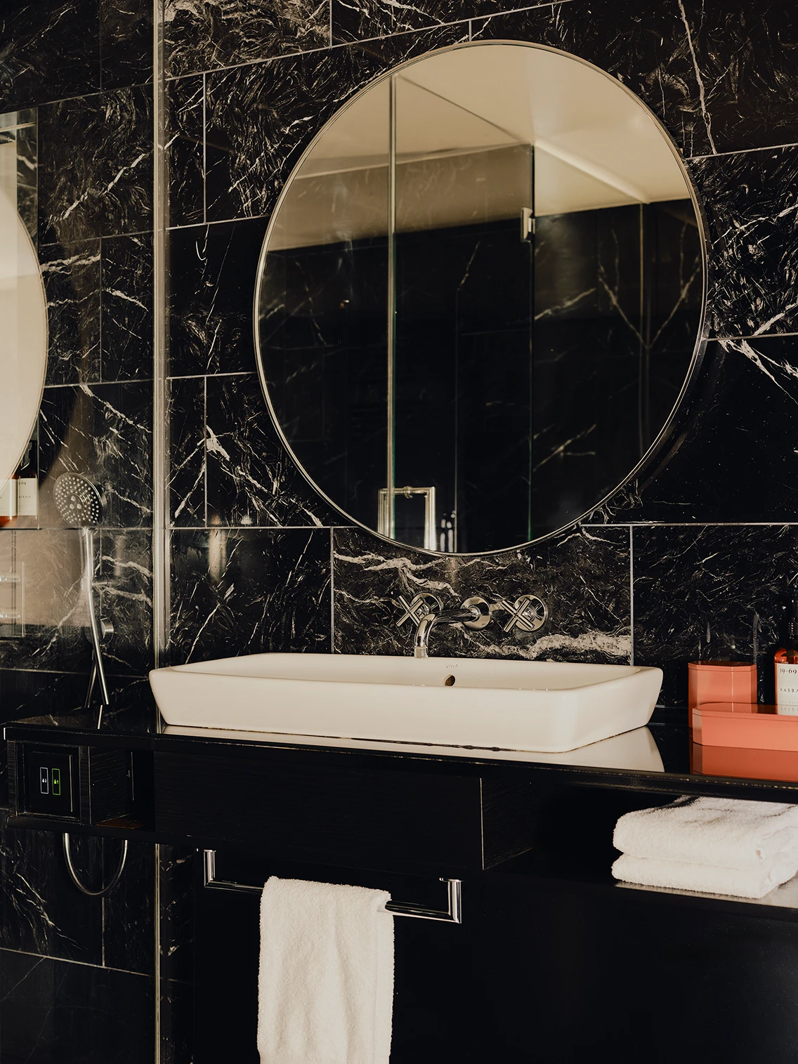 Modernes Badezimmer mit schwarzer Marmorwand, rundem Spiegel und weißem Aufsatzwaschbecken im Hotel The Dean München