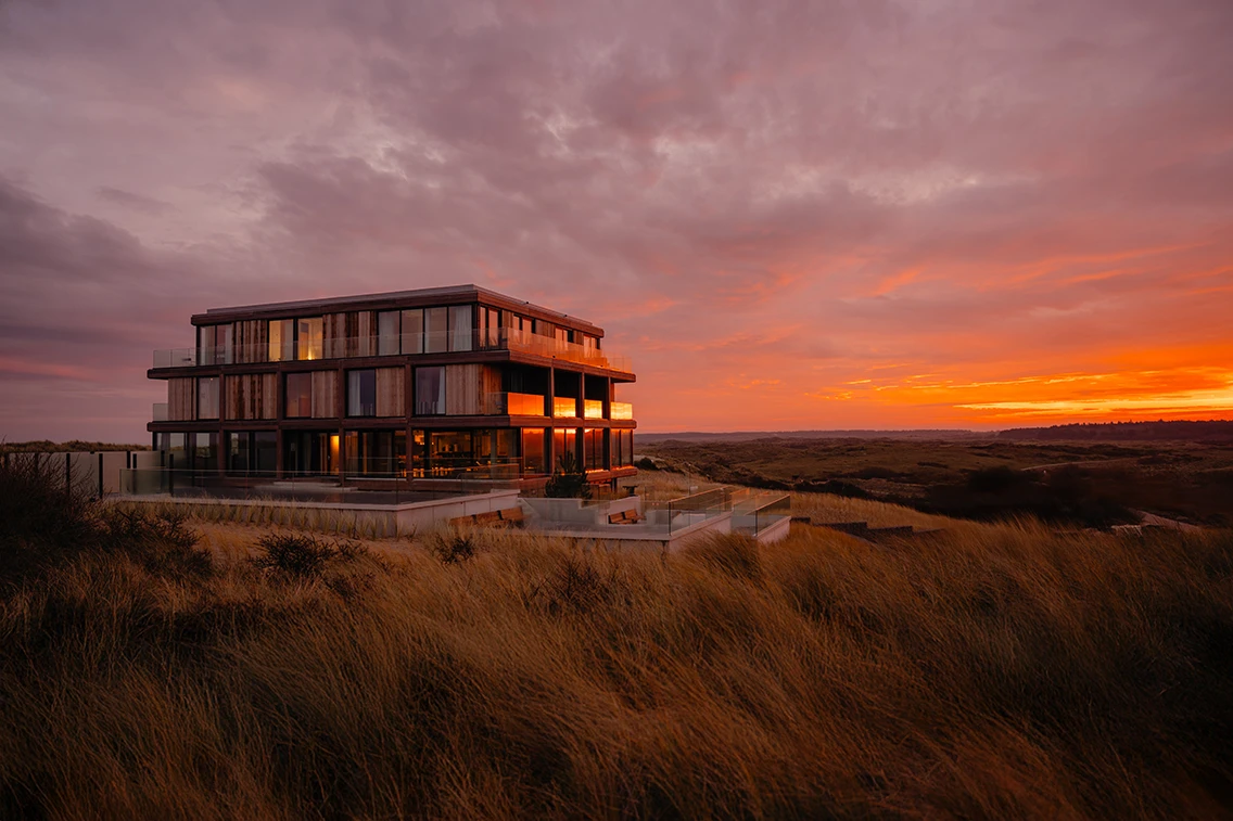 Das Hotel Elements Terschelling auf der Insel Terschelling vor einem spektakulären, orange-violetten Sonnenuntergang über der Dünenlandschaft. || © Chantal Arnts