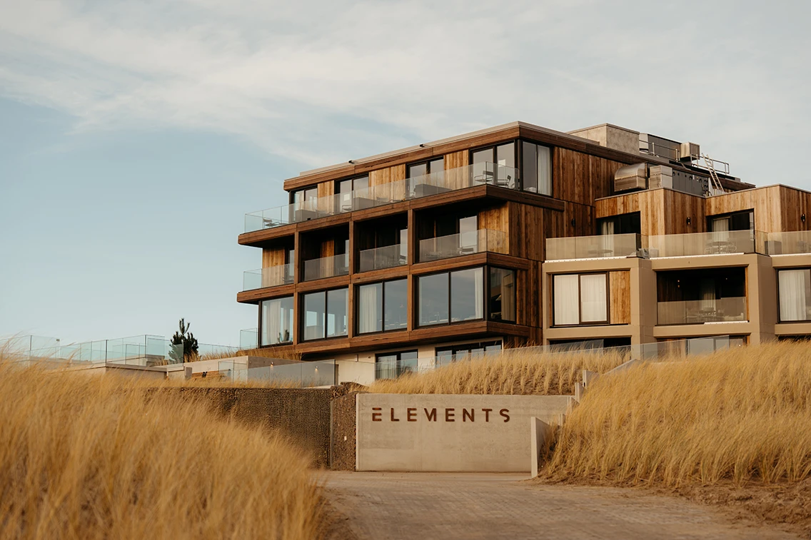 Zufahrt und Vorderansicht des Hotel Elements Terschelling mit Holz-Beton-Architektur und eingefrästem Schriftzug auf einer Betonmauer in den Dünen. || © Chantal Arnts