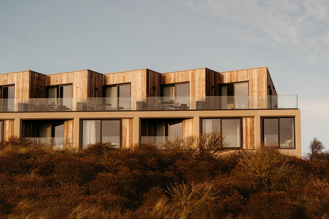 Holz- und Betonfassade des Hotel Elements Terschelling von Marc Koehler Associates mit verglasten Balkonen direkt in den Bewachsenen Dünen. || © Chantal Arnts