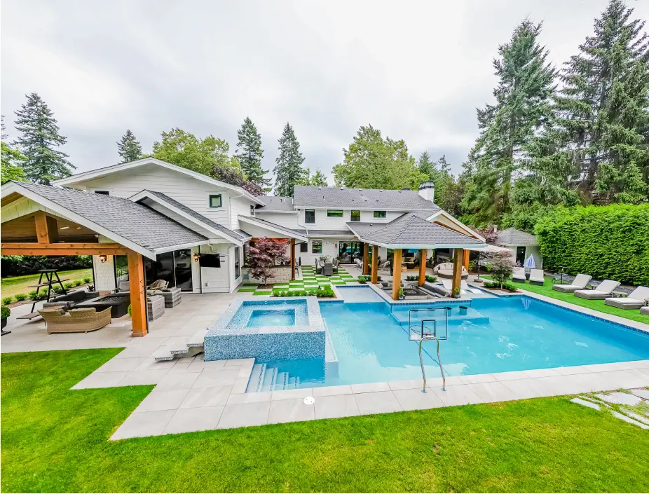 a concrete pool installed in the backyard of a house surrounded by beautiful garden