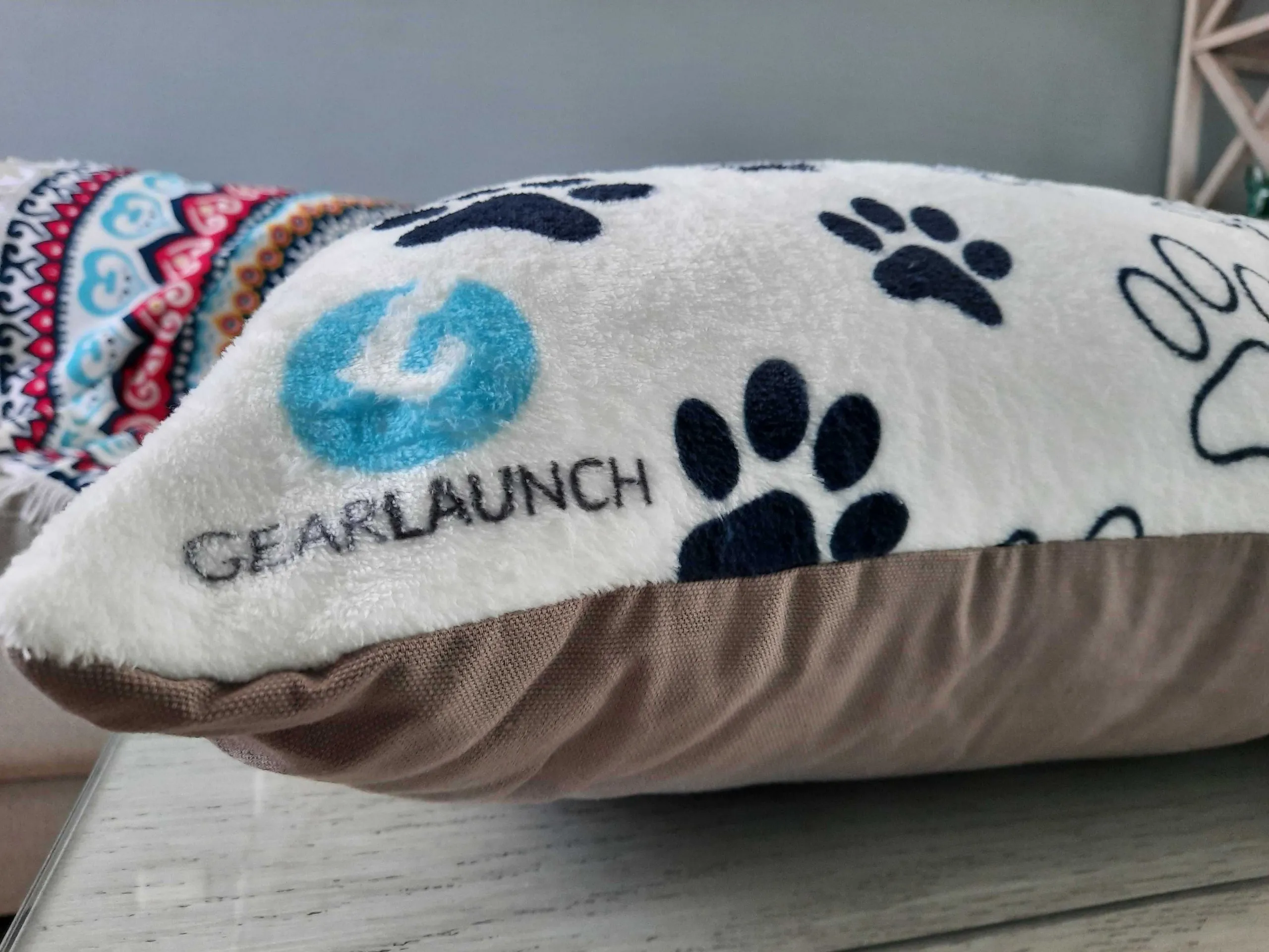 Close up of indoor pet bed, white background with black paw prints and GearLaunch Logo