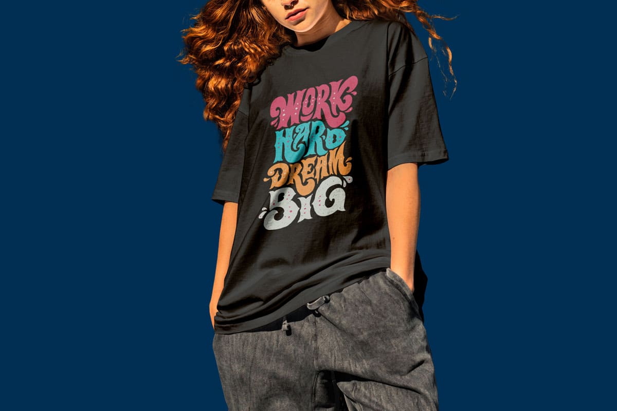 Young woman wearing oversized black T-shirt with colorful ‘Work Hard Dream Big’ graphic design – motivational custom apparel for print-on-demand