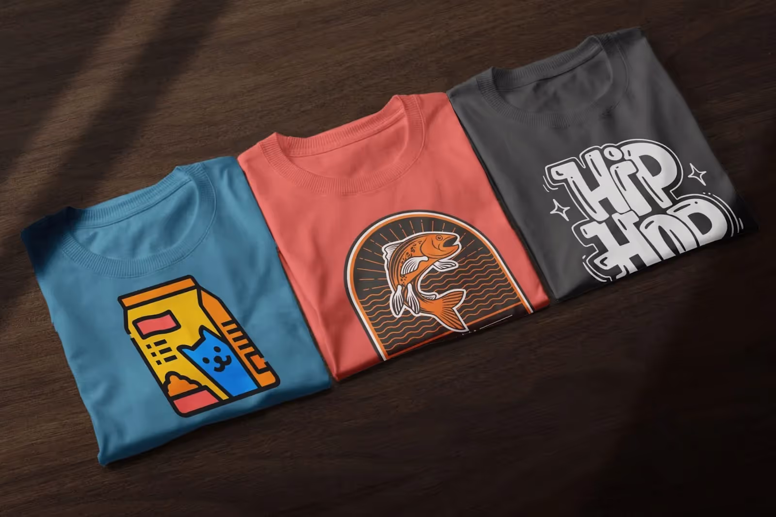 Three folded graphic T-shirts with cat milk carton, fish illustration, and hip hop typography – trendy custom designs for print-on-demand