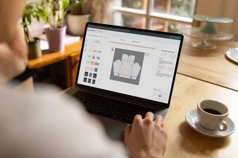 Designer creating Christmas print-on-demand product mockups on laptop, preparing POD artwork for GearLaunch platform.