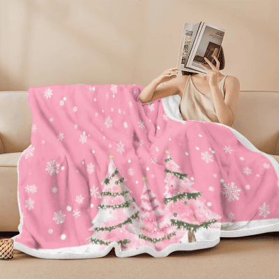 Woman reading a book while wrapped in a pink Christmas blanket with snowflakes and tree patterns — cozy lifestyle product photo for Q4 holiday marketing