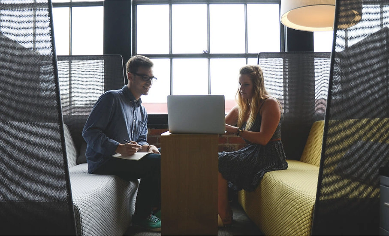 Two people talking over a laptop in a cosy meeting booth