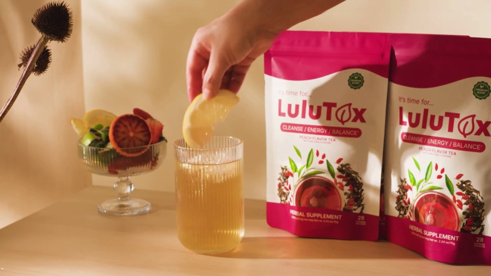 Two Lulutox Peach Flavor Tea pouches beside a glass of iced tea with lemon.